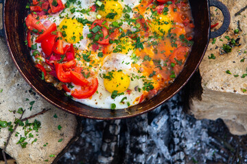 Eggs prepared with vegetables on a frying pan on the fire in the forest. Cooking scrambled eggs over an open fire. Breakfast in nature. Tourist food.