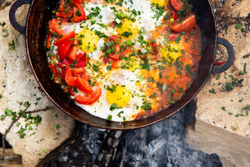 Eggs prepared with vegetables on a frying pan on the fire in the forest. Cooking scrambled eggs over an open fire. Breakfast in nature. Tourist food.