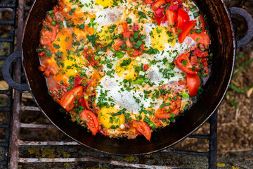 Eggs prepared with vegetables on a frying pan on the fire in the forest. Cooking scrambled eggs over an open fire. Breakfast in nature. Tourist food.