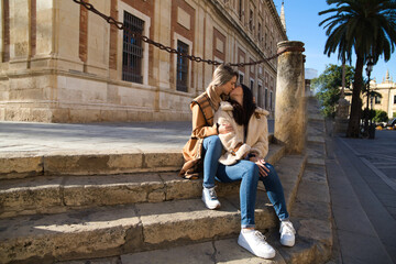 lesbian couple sitting on the steps of a pavement in a monumental square in old europe. They are very much in love and happy. Concept tourism and travel, lgtb. Rights and equality.