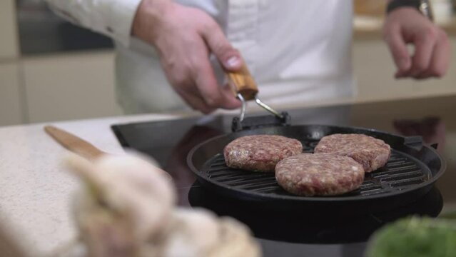 Cooking beefstakes patties for burger. Chef roasting fat meat cutlet for hamburger on a metal grill frying pan at restaurant kitchen. American unhealthy fastfood making.