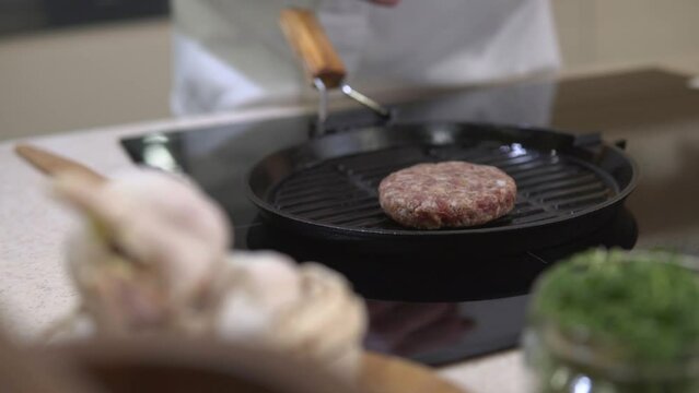 Cooking beefstake patty for burger. Chef roasting fat meat cutlet for hamburger on a metal grill frying pan at restaurant kitchen. American unhealthy fastfood making.