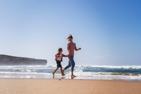 Happy mother and daughter running at beach on sunny day