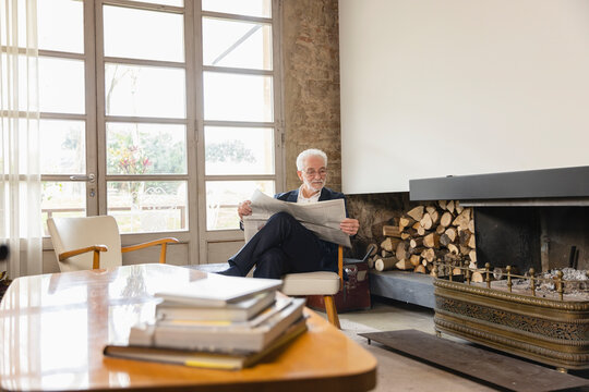 Man reading newspaper sitting on chair in living room at home