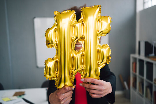 Businesswoman holding golden hashtag symbol balloon in front of face