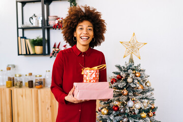 Happy woman with gifts standing by Christmas tree at home