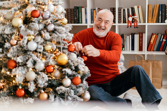 Smiling senior man decorating Christmas tree at home