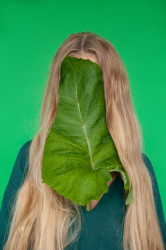 Woman hiding face with burdock leaf against green background