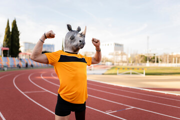 Man in rhinoceros face mask flexing biceps on running track