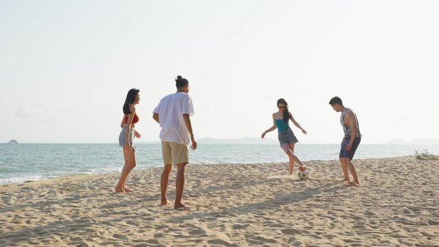 Group of Asian young man and woman play soccer on the beach together.