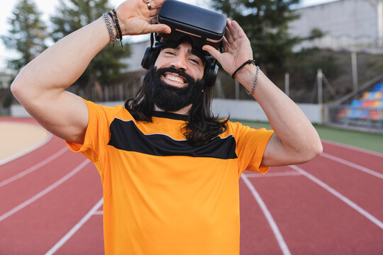 Happy man with virtual reality simulator standing on running track