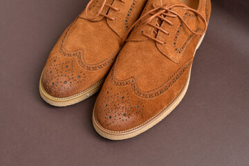 Pair of brown suede derby shoes on light brown background. Top view. Copy space. 