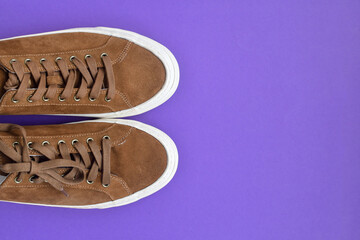 A pair of brown suede sneakers on purple background. Top view. Copy space.