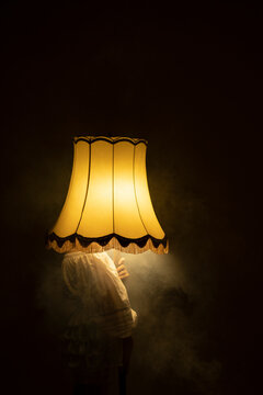 Young woman hiding face with smoky illuminated lamp in dark room