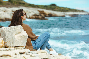 woman sitting on cliff enjoying view of the sea. windy weather. sunny day