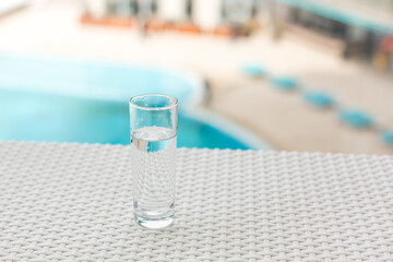 A glass of clean water in the open air. Glass glass with water on the background of the pool. Soft focus.