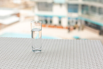 A glass of clean water in the open air. Glass glass with water on the background of the pool. Soft focus.