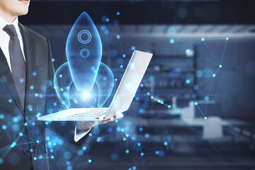 Close up of businessman hand holding laptop with abstract glowing blue rocket space ship on blurry...