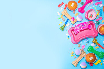 Pet happy birthday background with set different dogs snack, food and toys, bone-shaped dog bowl, birthday cupcakes with happy birthday candles and accessories. Flatlay on blue background top view