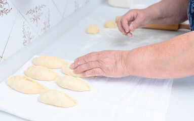 Senior woman hands making pies with apple filling on a white kitchen table with wooden rolling pin on background. Selective focus. Cooking at home concept. Tradition home-made food