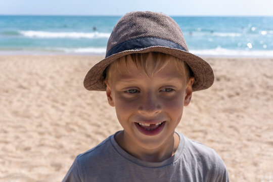 The boy laughs fervently against the backdrop of the sea. The child without a tooth smiles. Kid in a beach hat is happy. Happy holidays at sea. Dimples on the cheeks of a child - Powered by Adobe