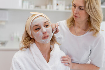 Obraz na płótnie Canvas Facial peeling mask, beauty spa, skin care. Woman getting facial treatment by beautician at SPA salon, side view, closeup. Anti-aging treatment. Cosmetology and professional face care