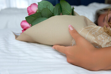 Girl sleeping in the room received bouquet of fragrant roses as gift. Surprise for sleeping wife in the form of a bouquet of delightful roses in a craft bag was made by a loving husband for a holiday
