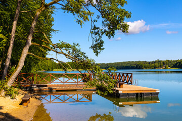 Wooded shore of Jezioro Gwiazdy lake with wooden jetty platform in Bukowo Borowy Mlyn Village near...