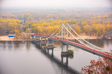 Autumn scenery with pedestrian Park Bridge, Trukhaniv island and Dnieper river in Kyiv, Ukraine in morning mist