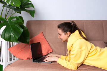 Young woman working remotely from home on a laptop while sitting on the couch. The concept of remote work and online learning.