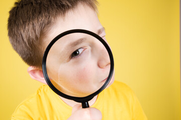 Closeup of boy looking at camera through loupe or magnifying glass isolated on yellow background.