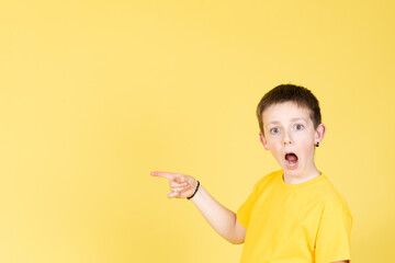 Surprised boy looking at camera and pointing to yellow copy space