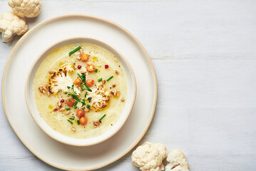 Vegan cauliflower soup on white background. Healthy vegan cauliflower soup served in bowl on white table. - obrazy, fototapety, plakaty