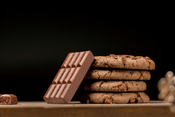 brown chocolate chip cookie large poan.  On a black background. Chocolate chip cookies with brown chocolate chips are placed on a wooden table.