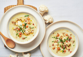 Vegan cauliflower soup on white background. Healthy vegan cauliflower soup served in bowl on white table.