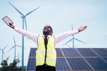 African engineer stand holding tablet front solar photovoltaic and wind turbines generating...