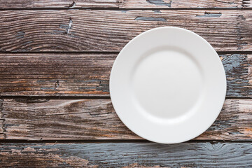Plate on the background of a wooden tabletop. View from above. Small flat round white plate. Place for text.