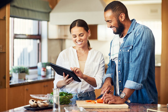 I Found A New Recipe We Should Try. Shot Of A Young Couple Using A Digital Tablet While Cooking At Home.