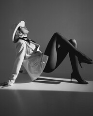Fashion shoot. Portrait of a beautiful elegant sexy girl in a white hat and jacket. Long legs in pantyhose and shoes.
