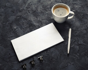 Obraz na płótnie Canvas Photo of blank paper envelope, coffee cup, pen and metal clips on black plaster background. Blank stationery set.
