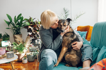 Woman cuddling and playing with her dog at home on the couch