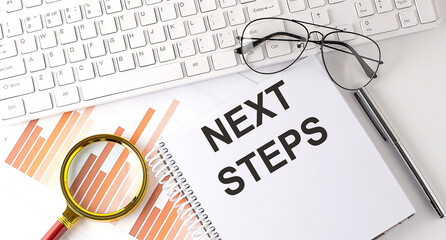 NEXT STEPS text written on notebook with keyboard, chart,and glasses