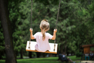child swings on swing in park in summer.