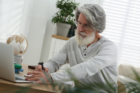 Middle Aged Man With Laptop And Notebook Learning At Table Indoors