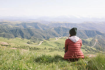 Naklejka na ściany i meble woman is sitting against background of mountains . travel, hiking, journey, outdoor recreation