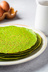 Stack of spinach crepes on plate. Green vegan pancakes, gray background. Healthy breakfast recipe.