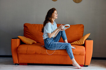 woman on the orange sofa listening to music with headphones Lifestyle