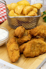 potato with cooked chicken nuggets on a wooden board with a pot of sauce