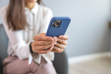 Woman in casuals seating in office by a window with phone in hand. Businesswoman with mobile phone in hand. Shot of a businesswoman using technology at work