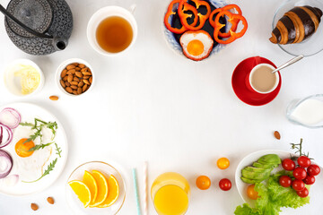 Delicious family breakfast table with coffee, tea, orange juice, croissants, toast, butter, fried and boiled eggs, avocado, cherry tomatoes, almond and salad. Copy space.
